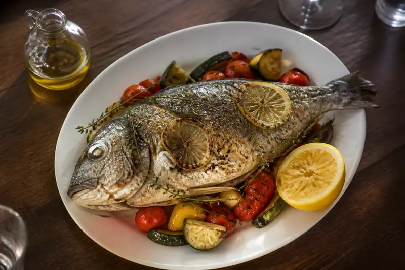 Loup de mer entier rôti dans une assiette blanche, garni de citron, de thym et de légumes grillés.